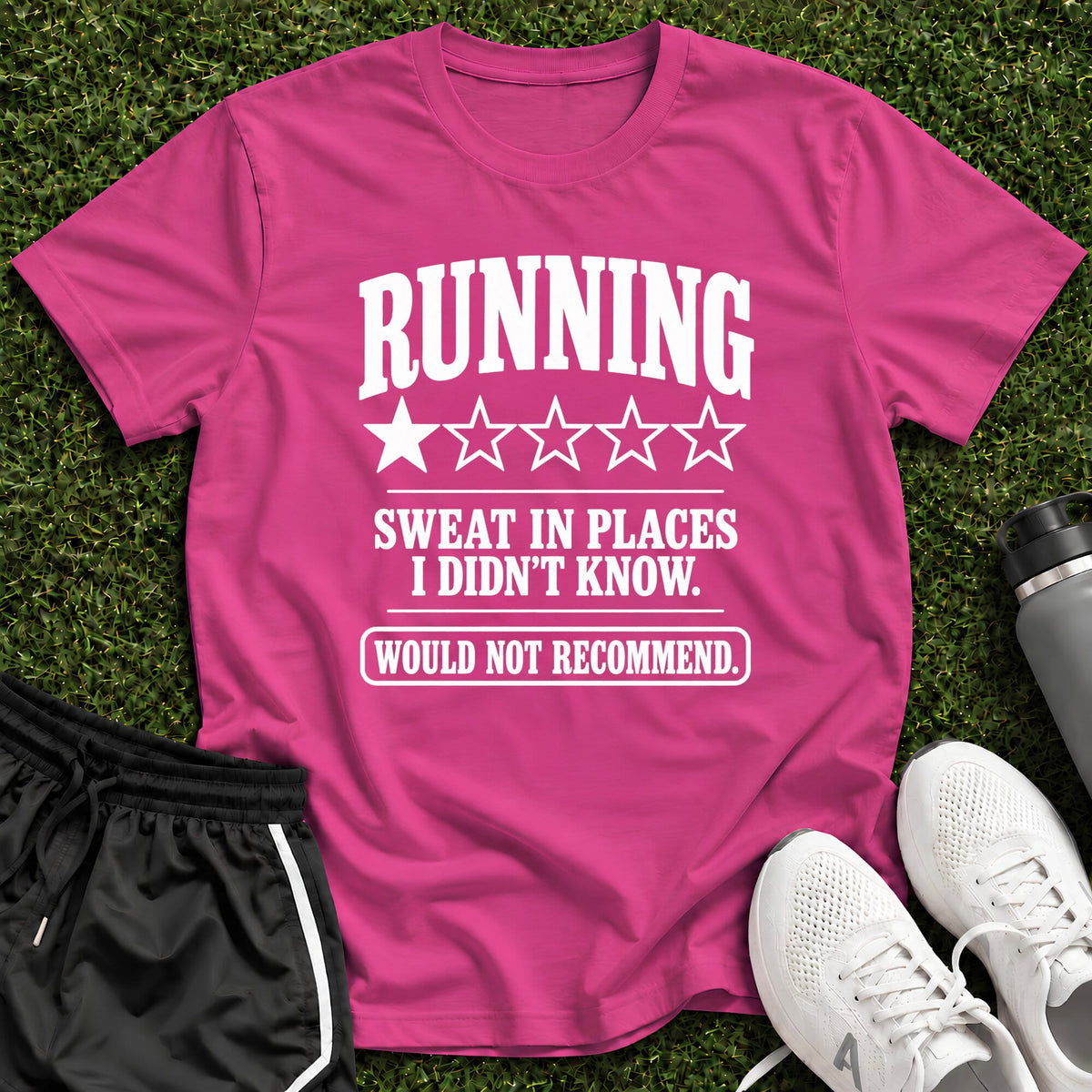 A bright pink graphic t-shirt laid flat on green grass, featuring the white text 'RUNNING SWEAT IN PLACES I DIDN'T KNOW. WOULD NOT RECOMMEND.