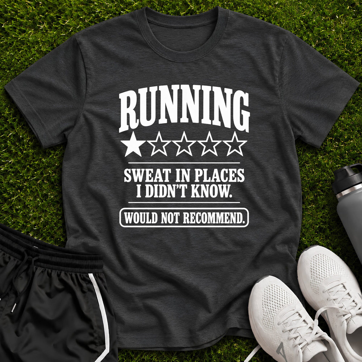 A dark charcoal gray graphic t-shirt laid flat on green grass, featuring the white printed text 'RUNNING SWEAT IN PLACES I DIDN'T KNOW. WOULD NOT RECOMMEND.