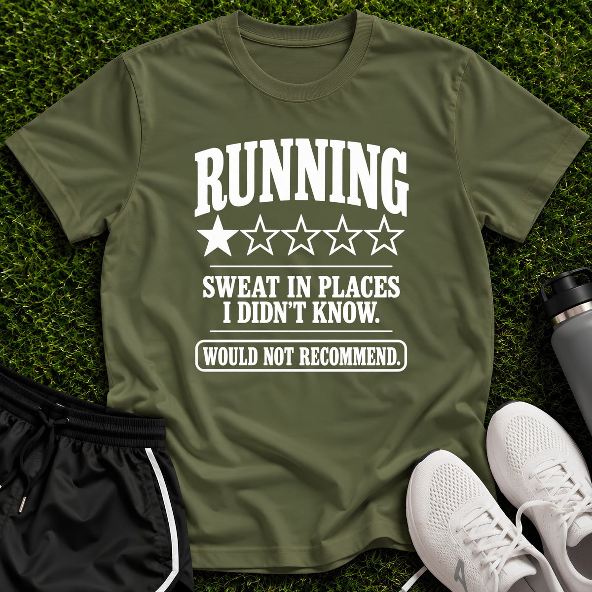 An olive green graphic t-shirt laid flat on a green grass background, styled with black athletic shorts, white sneakers, and a gray water bottle. The t-shirt features a white graphic that reads 'RUNNING SWEAT IN PLACES I DIDN'T KNOW.
